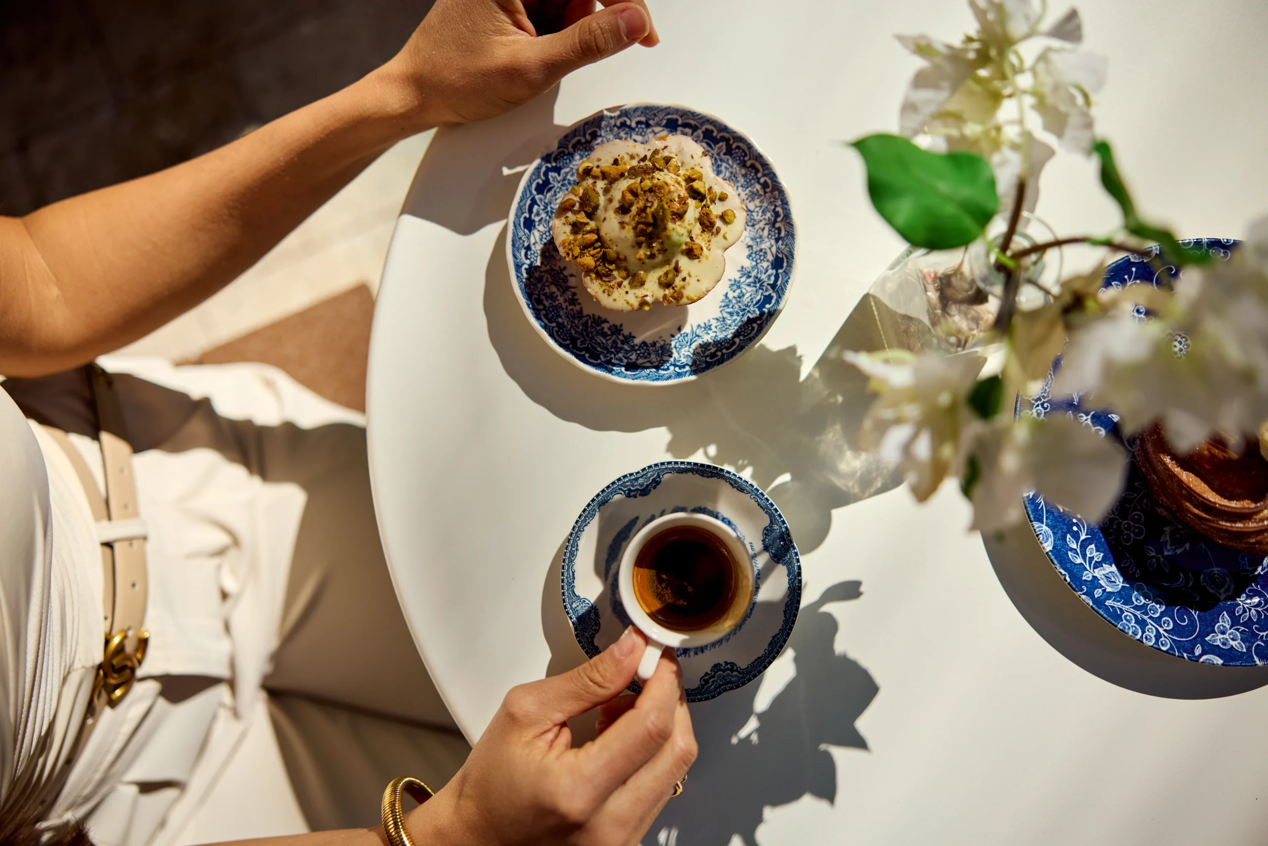 Outdoor table with coffee, dessert, blue patterned dishes, flowers, and sunlight