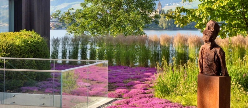 Garden landscape with sculptural artwork, colorful planting, lake views, and natural greenery by ENEA