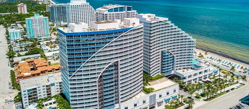 Aerial view of an oceanfront resort with modern glass towers, beach access, and turquoise Atlantic water