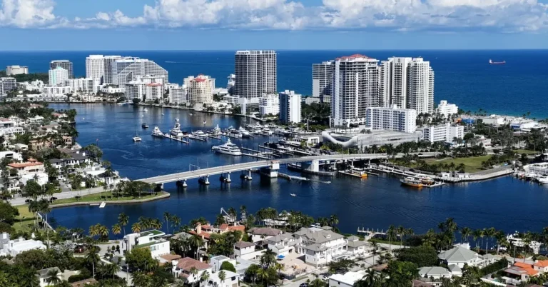 Aerial view of Fort Lauderdale's waterfront real estate, showcasing luxury high-rise condos, marina, and Intracoastal Waterway with the Atlantic Ocean beyond.