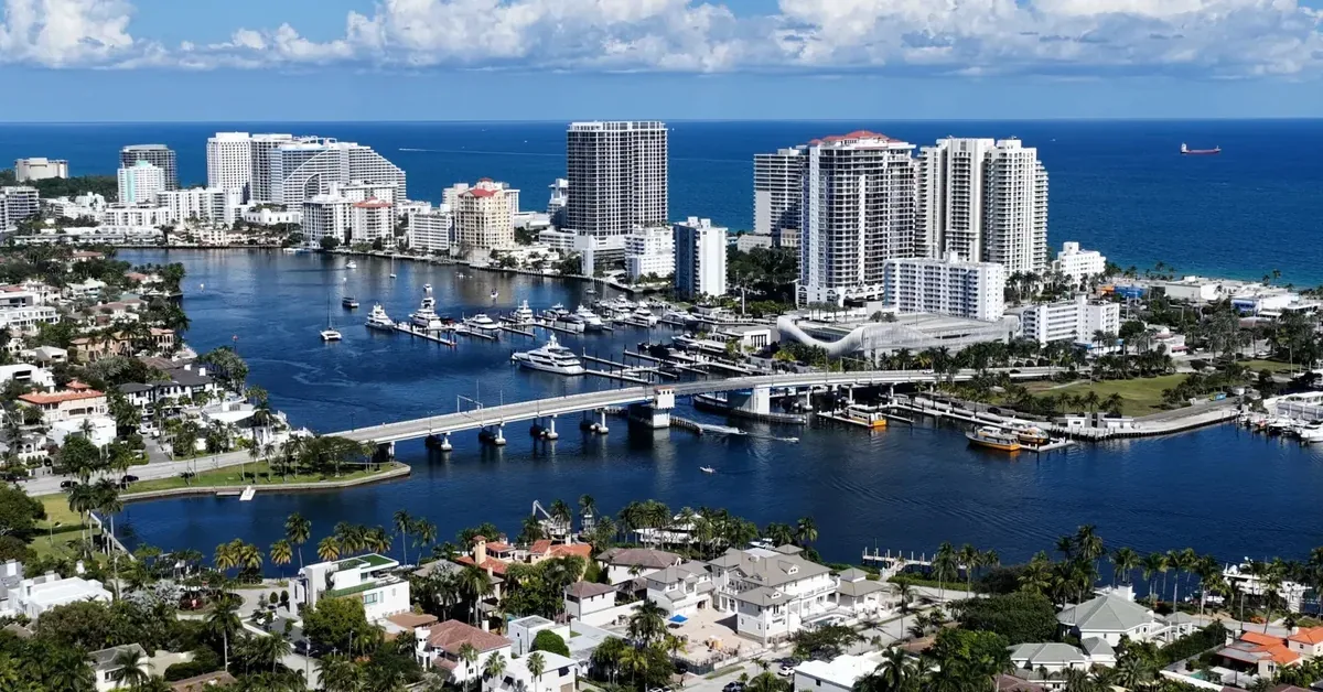 Aerial view of Fort Lauderdale's waterfront real estate, showcasing luxury high-rise condos, marina, and Intracoastal Waterway with the Atlantic Ocean beyond.