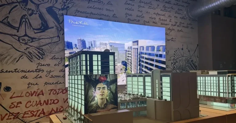 Architectural scale model of the Frida Kahlo-themed mixed-use development displayed alongside a digital rendering and artistic murals in Spanish.