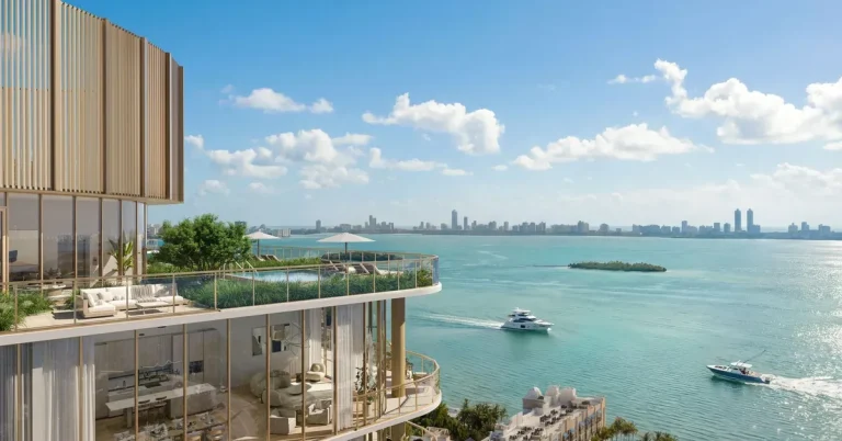 Luxury waterfront high-rise with curved gold-accented balconies overlooks turquoise Biscayne Bay with Miami skyline and passing yachts in the distance.