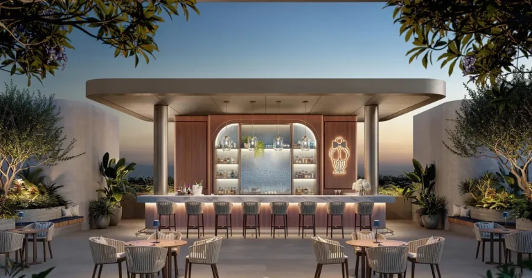 Elegant outdoor bar and lounge area at dusk featuring warm ambient lighting, bar seating, and lush tropical landscaping at a luxury resort property.